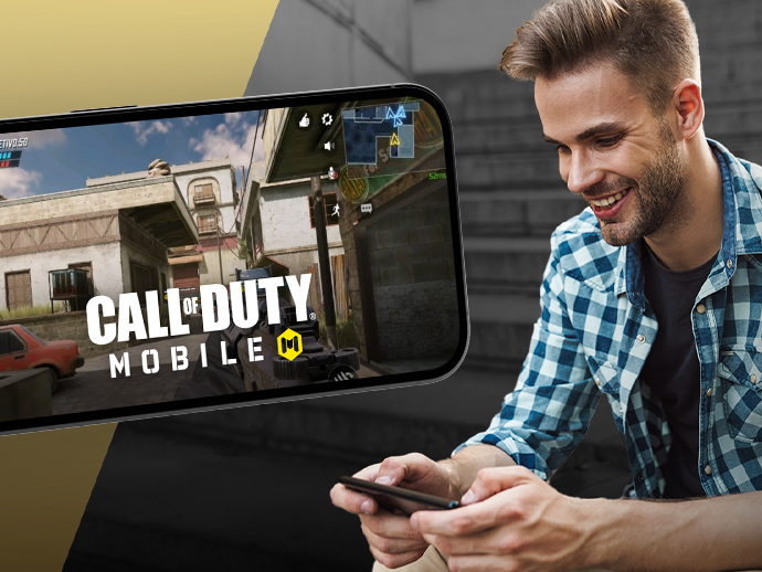 Ein junger Mann spielt Call of Duty: Mobile auf seinem Smartphone, darüber ist ein Bildschirm ein eingeblendet. 