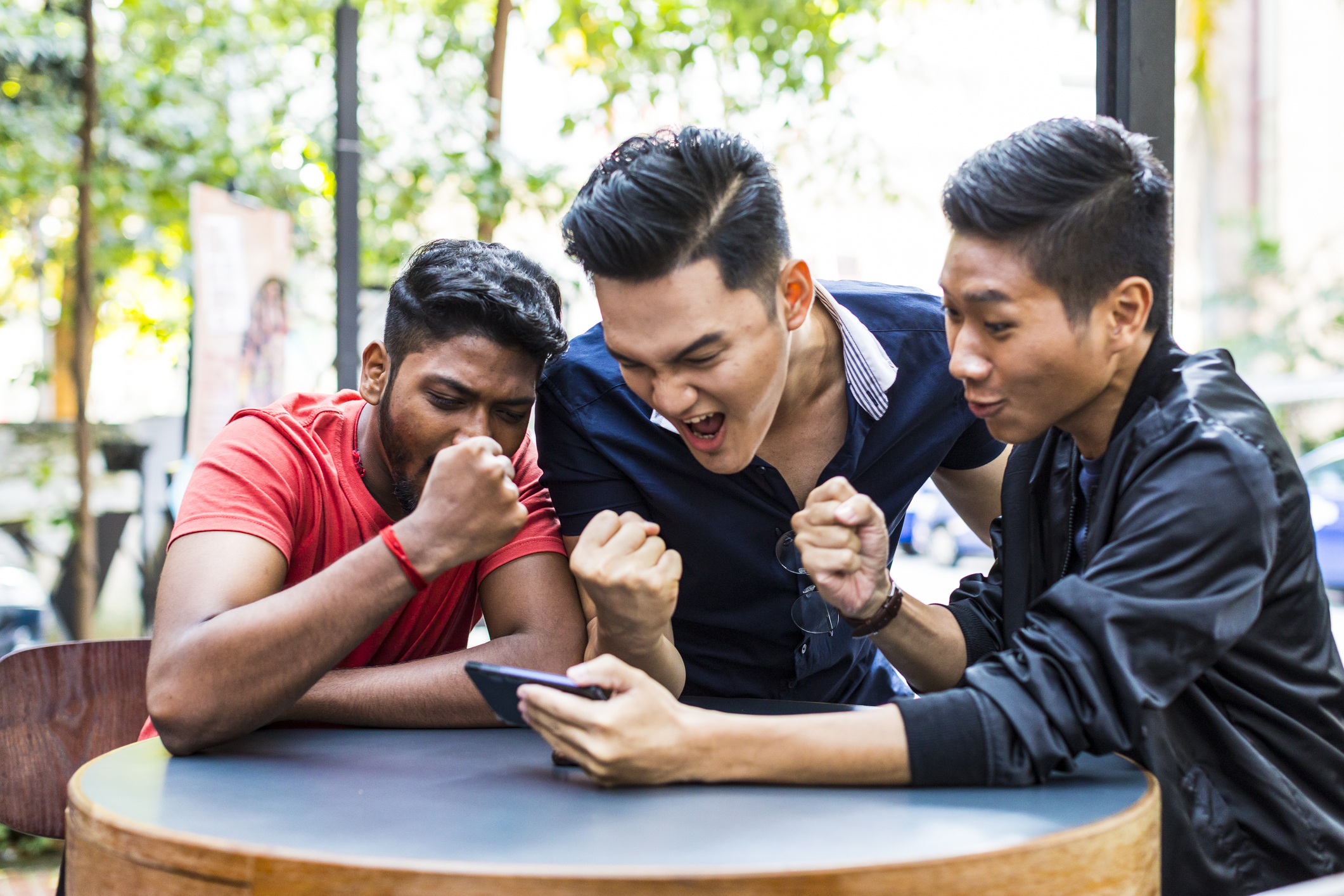 Eine Gruppe von Freunden feiert ein Spiel, das sie sich gemeinsam auf dem Handy ansehen. 