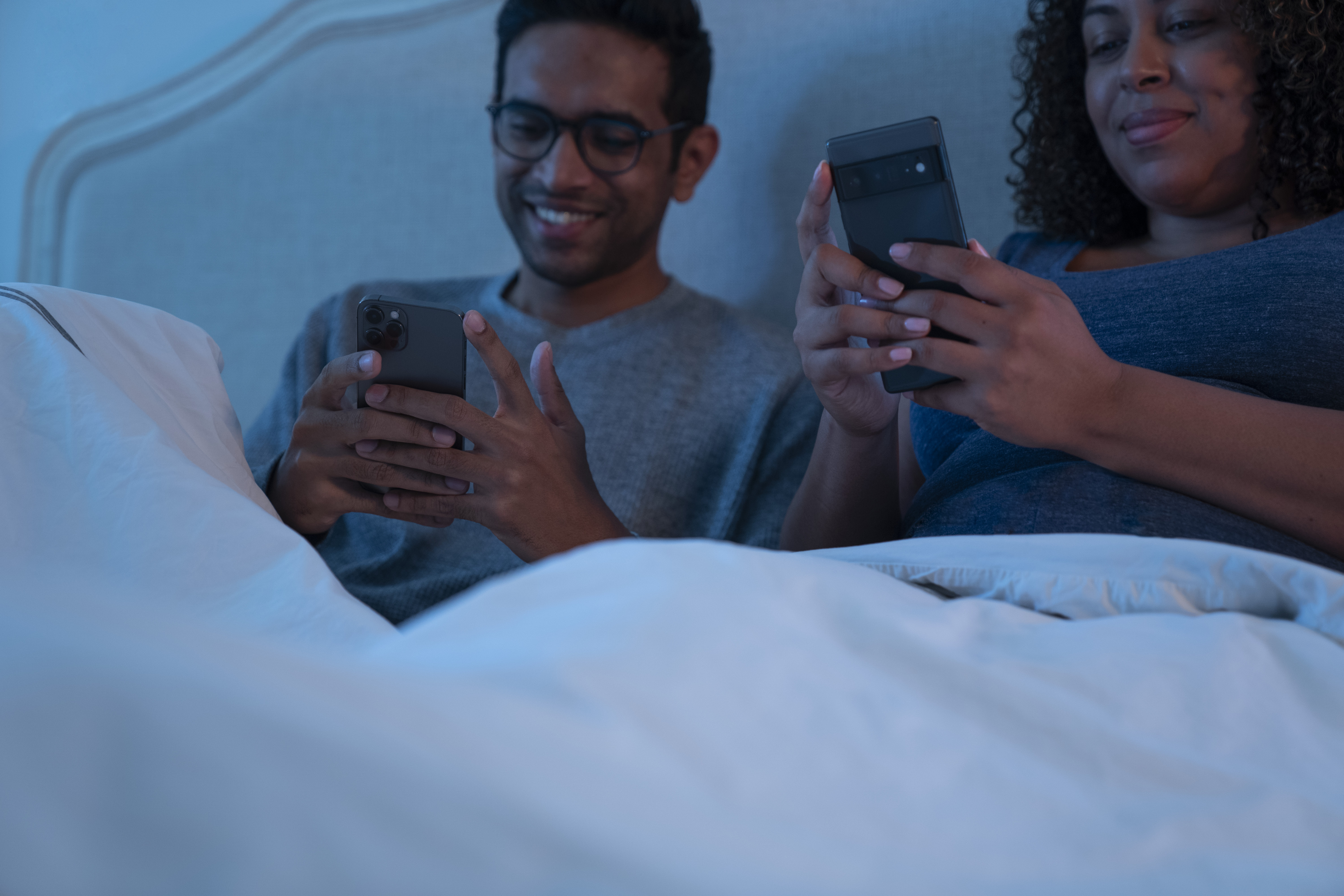 A couple play mobile games together in their bedroom.