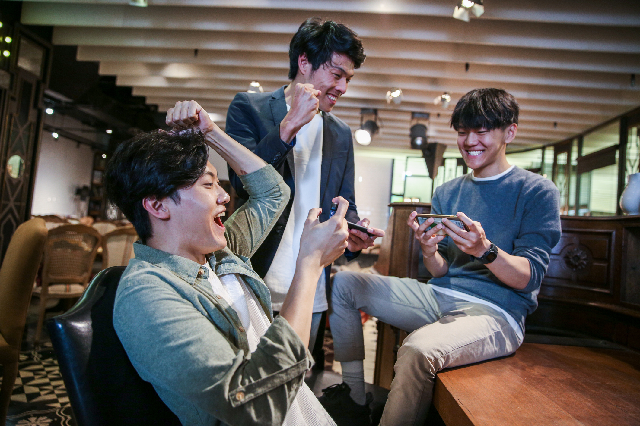 Three guys playing games on their phones and celebrating.