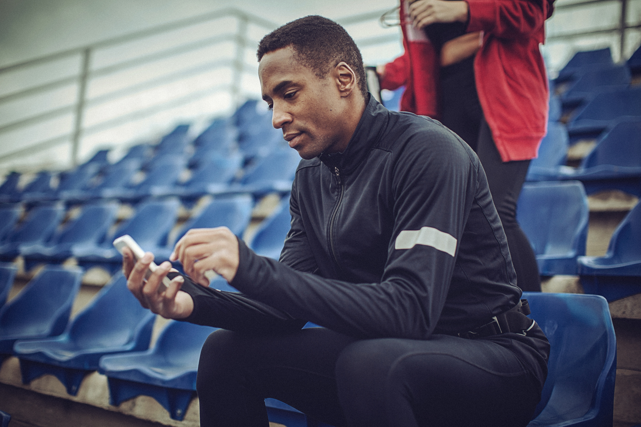 An athlete plays on his phone while seated in a stadium.