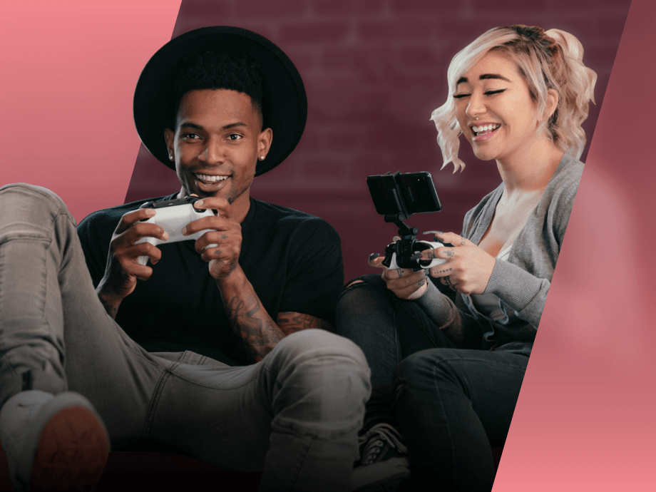 A happy young man plays XBOX while a young woman plays on a mobile phone next to him. 